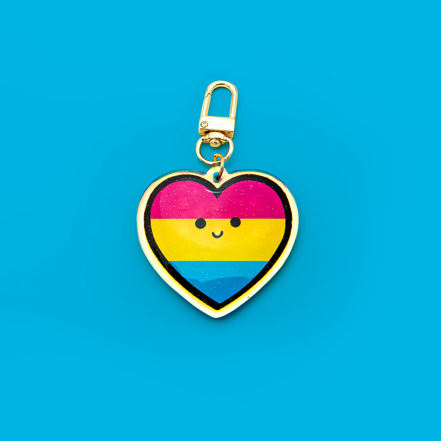 A 2-inch rainbow acrylic keychain featuring double-sided printing, epoxy glitter on the front, and a gold rounded clip hook. Inspired by the inclusive pride flag symbolizing attraction to all genders.